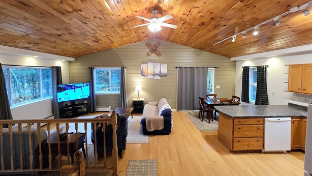 A cozy cabin interior with a wooden ceiling, a TV in the living area, a dining table, and a kitchen with wooden cabinets. - Valley Home with Game Room, Walking Distance to Narrow Gauge Trails & Restaurant (Carrabassett Valley)