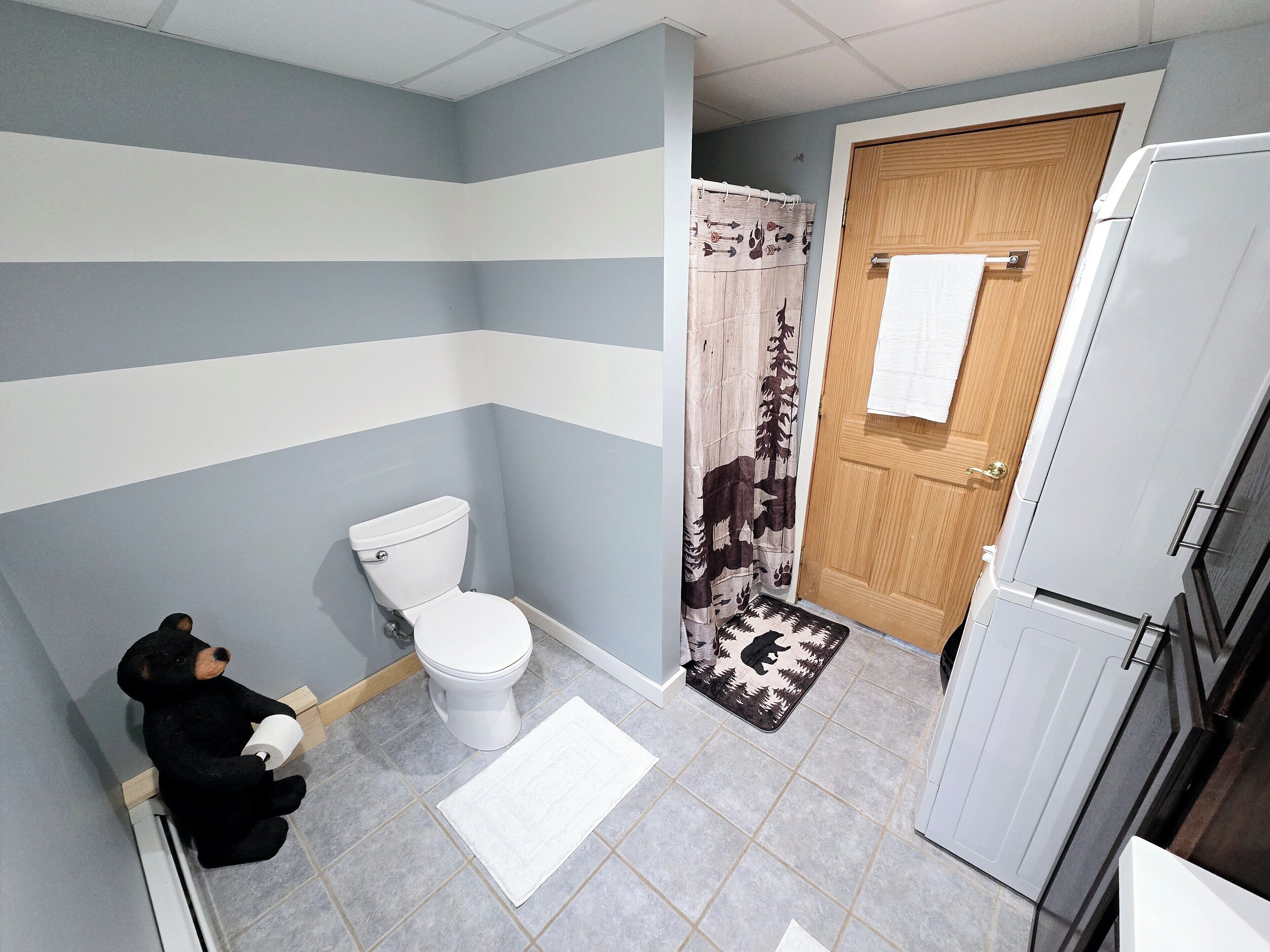 Un baño con inodoro, cortina de ducha, puerta de madera y una toalla blanca colgada en la puerta.