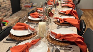 A long dining table set with white plates, orange napkins, and clear glassware.