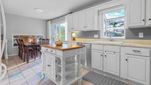 A kitchen with white cabinetry, a wooden island, and a dining area with a table and chairs.