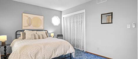 A bedroom with a bed, a ceiling fan, a window with curtains, and a wall-mounted light fixture.