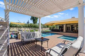 A covered outdoor area with a pool, lounge chairs, and a barbecue area.