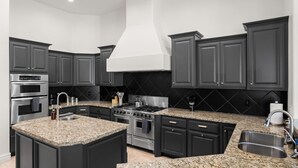 Una cocina moderna con muebles oscuros, encimeras de granito, electrodomésticos de acero inoxidable y una isla central.