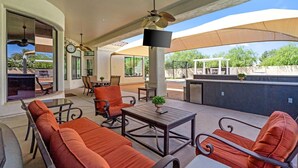 Un patio techado al aire libre con asientos, un televisor y una piscina.