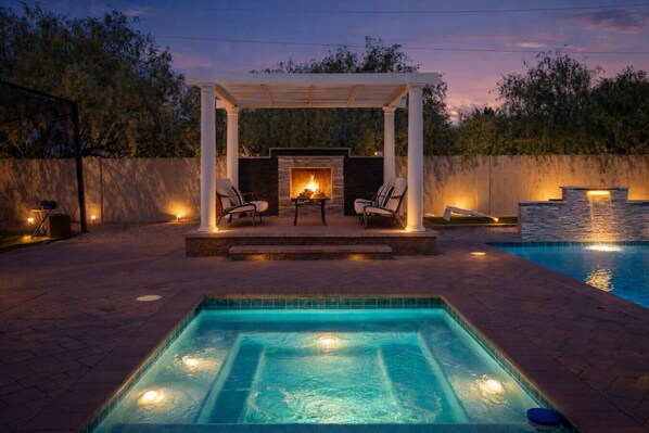 A pool area with a hot tub, seating, and a pergola.