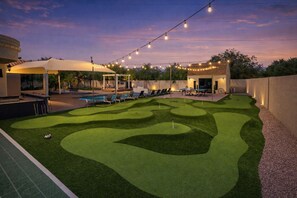 A backyard with a pool, artificial grass, lounge chairs, and string lights.