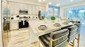 A modern kitchen with white cabinetry, stainless steel appliances, and a central island with seating. - Amazing 8Br /Private Pool  & hot tub 2547 (kissimmee)