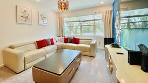 A living room with a beige sectional sofa, a coffee table, and a desk with a computer. There are framed pictures on the wall and a large window with curtains. - Amazing 8Br /Private Pool  & hot tub 2547 (kissimmee)