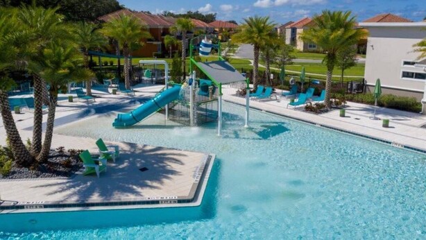 A pool area with a water slide, lounge chairs, and palm trees. - Amazing 8Br /Private Pool  & hot tub 2547 (kissimmee)