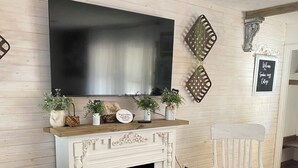 A cozy living room with a fireplace, a mounted TV, and a comfortable seating area. - Charming cottage in Girard with WiFi and AC - perfect getaway (Girard)
