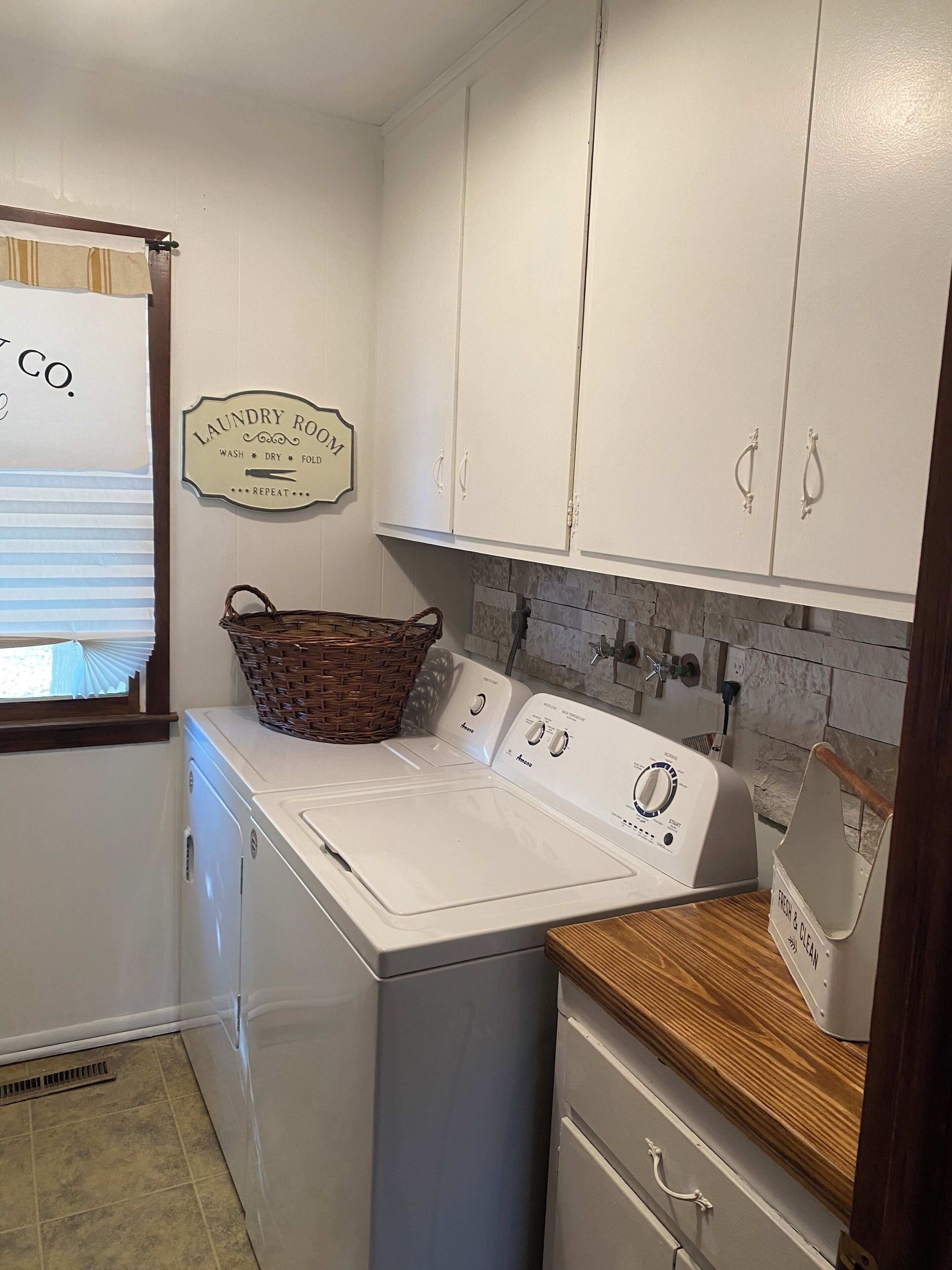 A laundry room with a front-loading washer and dryer, a wicker basket, and a sign that says "Laundry Room Wash, Dry, Fold, Repeat."