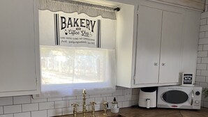 A kitchen with white cabinets, a wooden countertop, a sink with gold faucets, and a window with a decorative curtain. - Charming cottage in Girard with WiFi and AC - perfect getaway (Girard)
