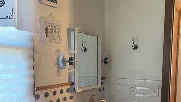 A bathroom with a wooden vanity, a white sink, and a mirror above it. There are towels hanging on the wall and a sign that says "Fresh Soap & Towel Service Free 5¢".