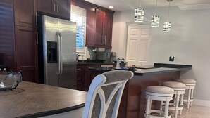 A modern kitchen with dark wooden cabinets, a stainless steel refrigerator, a dining table with a white chair, and a bar area with stools. - 3 bedroom 2 bath heated pool, 1 block to Wilton Dr close to Beaches
  Sleeps 6 (Wilton Manors)