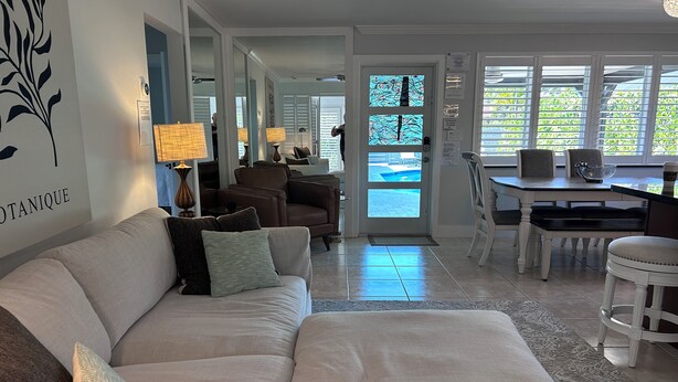 A living room with a sofa, a coffee table, and a dining area with a table and chairs. There is a door leading to a pool area. - 3 bedroom 2 bath heated pool, 1 block to Wilton Dr close to Beaches
  Sleeps 6 (Wilton Manors)