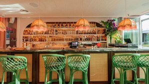 Zona bar con sgabelli verdi, una selezione di bottiglie sugli scaffali e lampade a sospensione.