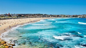 Una spiaggia costiera con acque blu cristalline, una riva sabbiosa e un panorama urbano sullo sfondo.