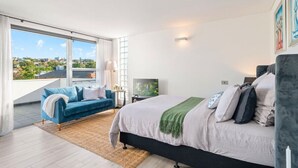 Una camera da letto moderna con un grande letto, un divano, una TV e un balcone con vista sulla città.