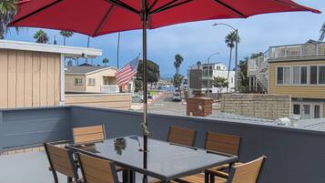 A rooftop terrace with a glass table and chairs, a red umbrella, and an American flag.