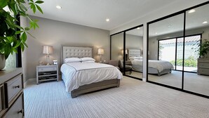 Een moderne slaapkamer met een groot bed, nachtkastjes, een spiegel en uitzicht door een glazen deur.