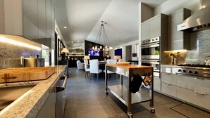 Een moderne keuken met een centraal eiland, roestvrijstalen apparatuur en een eethoek met witte stoelen.