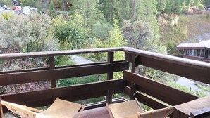 Un pontile in legno con due sedie pieghevoli e vista su una zona boschiva, con un edificio sullo sfondo.