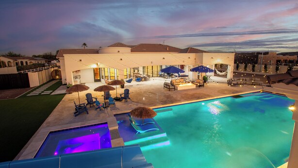 A swimming pool with lounge chairs and umbrellas, surrounded by a building with a patio area. - The Grand Oasis – Resort-Style Retreat w/ Sauna, Cold Plunge, Mini Golf & Volleyball (Goodyear)