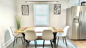 Un comedor con una mesa de madera, cuatro sillas, una ventana con persianas y un refrigerador de acero inoxidable.