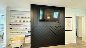 Una sala de estar moderna con televisor empotrado, pared con motivo de espiga, estantería y un pequeño banco de madera.