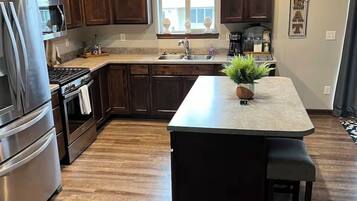 A kitchen with wooden cabinets, stainless steel appliances, a central island with seating, and a window providing natural light.