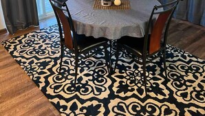 A dining area with a round table, four chairs, a chandelier, and a patterned rug.