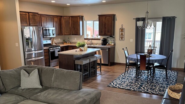 A modern kitchen with a refrigerator, microwave, and stove, a dining area with a table and chairs, and a living room with a sofa and a TV.