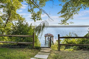 A wooden pathway leading to a gazebo by a lake with a clear view of the water and distant land.