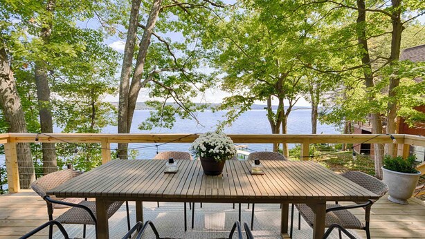 Une terrasse en bois avec une table et des chaises, donnant sur une étendue d’eau et entourée d’arbres.