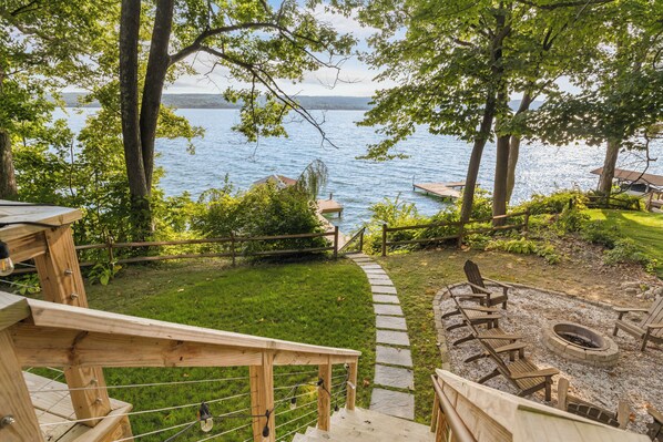 A deck with a stone pathway leading to a seating area with a fire pit, overlooking a lake.