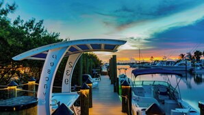 A wooden dock leading to a marina with boats docked, a covered seating area, and a sunset in the background. - New!Luxurious & spacious waterfront 4 bedroom house in Marathon with endless fun (Marathon)