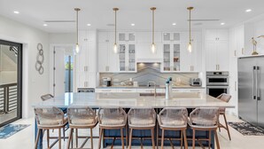 A modern kitchen with white cabinetry, a central island with bar stools, pendant lighting, and stainless steel appliances. - New!Luxurious & spacious waterfront 4 bedroom house in Marathon with endless fun (Marathon)
