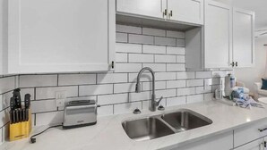 Una cocina moderna con armarios blancos, un lavamanos de acero inoxidable y un tostador.