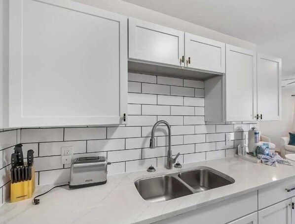 Una cocina moderna con armarios blancos, un lavamanos de acero inoxidable y un tostador.