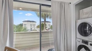Un balcón con vistas a edificios y palmeras, una lavadora y una silla.