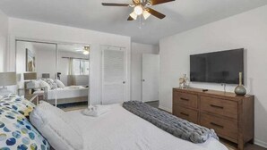 Un dormitorio con una cama, un tocador, un televisor y un ventilador de techo.