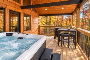 Una cabaña de madera con hidromasaje, mobiliario exterior y vistas a árboles otoñales.