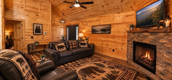 A log cabin interior with a fireplace, leather sofa, and a television mounted on the wall. - WEARS VALLEY-CLOSE TO ALL ATTRACTIONS! 2 BR 2 BA LOG CABIN, Sleeps 6!"LAZY BEAR" (Pigeon Forge)