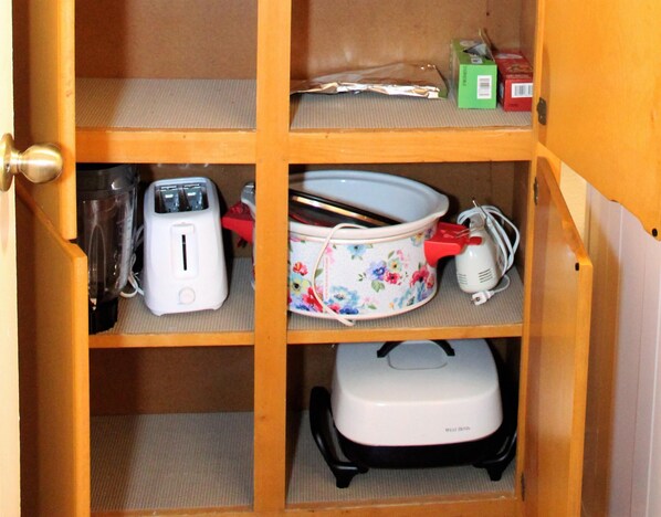 A kitchen cabinet with a toaster, a slow cooker, and a kettle.