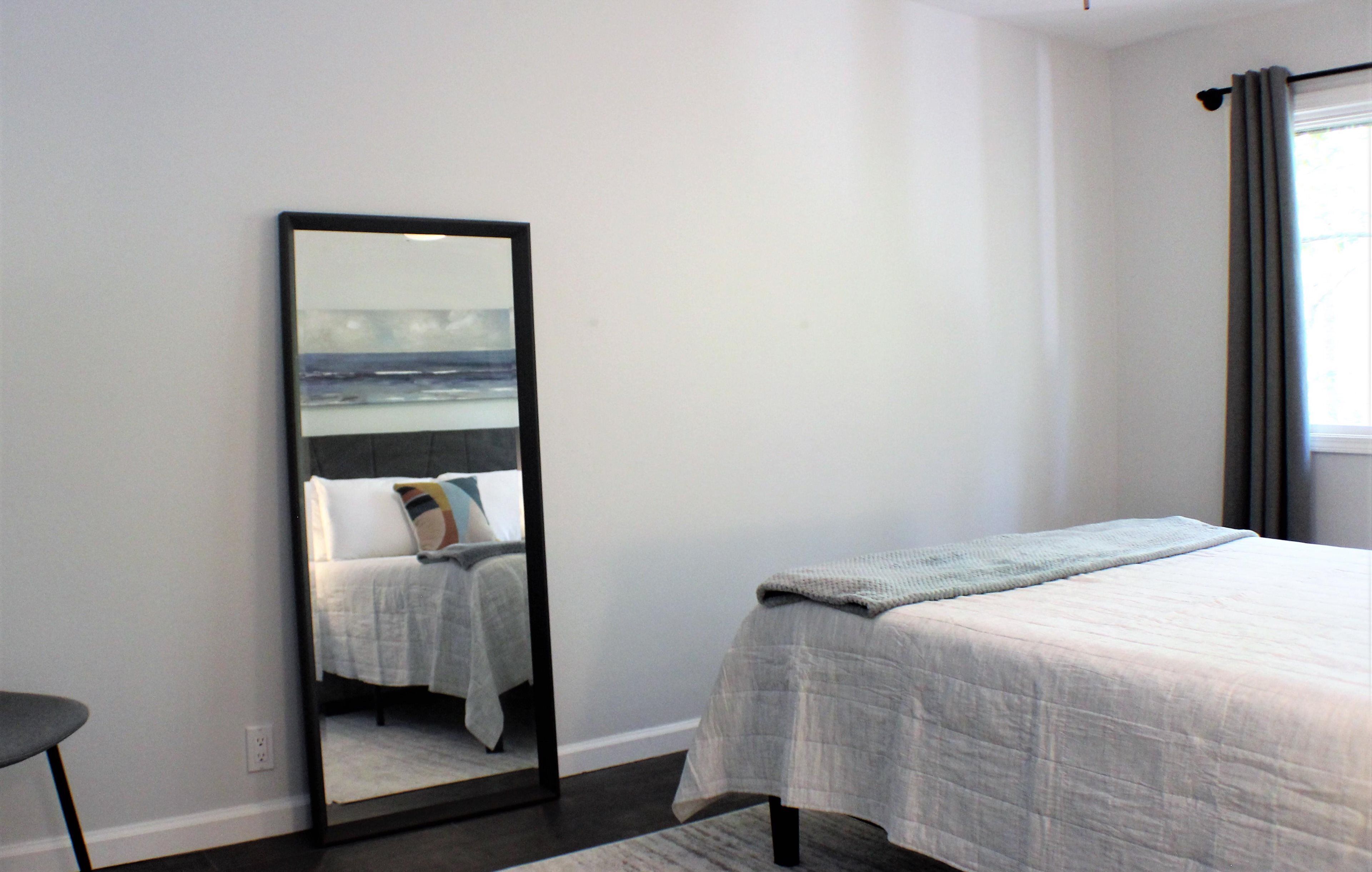 A bedroom with a bed, a mirror, and a window with curtains.