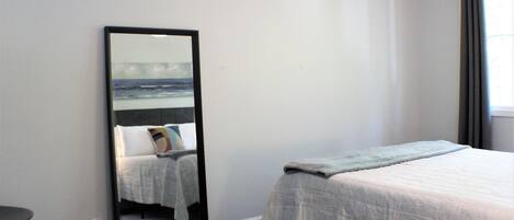 A bedroom with a bed, a mirror, and a window with curtains.
