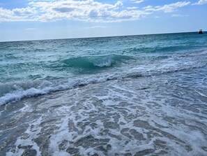 Une plage où les vagues se brisent près du rivage, un ciel dégagé et un bateau au loin.