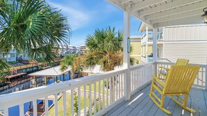 A balcony with white railings, a wooden rocking chair, and a view of a water body and buildings. - "Mermaid Cove" offers canal views, fenced-in yard, boat parking, pet friendly! (Mexico Beach)