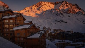 Eine Holzhütte mit Balkonen vor einer verschneiten Berglandschaft.
