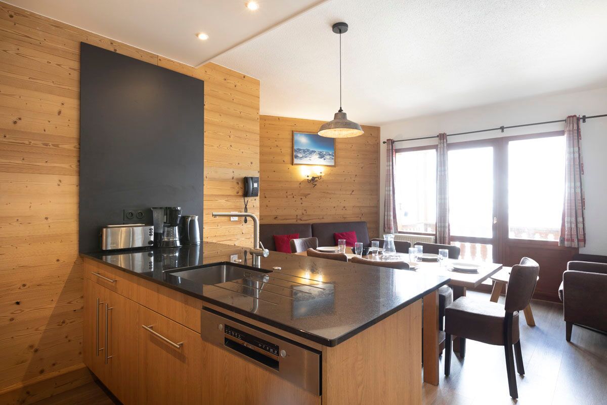 Une cuisine moderne dotée d’un îlot central, de murs recouverts de panneaux en bois et d’un coin repas avec un canapé et des chaises.